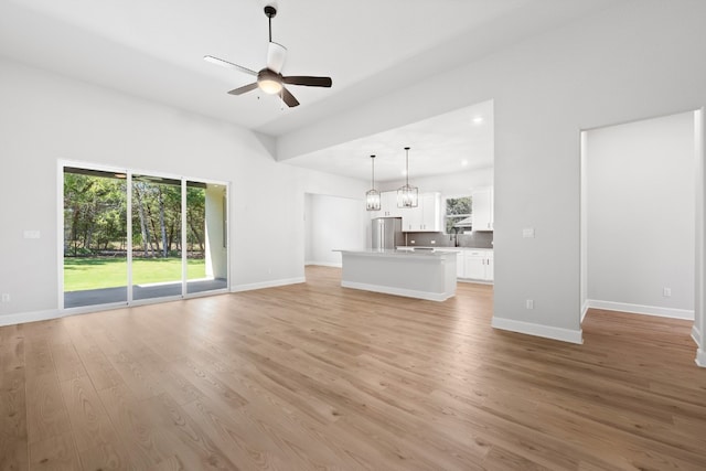 unfurnished living room featuring ceiling fan with notable chandelier, sink, and light hardwood / wood-style flooring