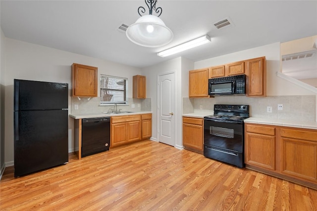 kitchen featuring sink, light hardwood / wood-style flooring, hanging light fixtures, and black appliances