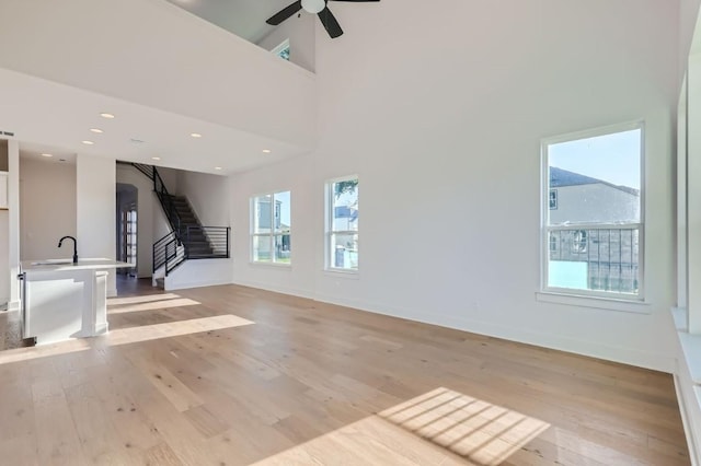 unfurnished living room with a towering ceiling, ceiling fan, sink, and light hardwood / wood-style floors