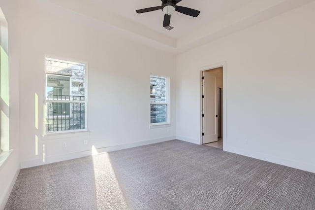 unfurnished room featuring a raised ceiling, light carpet, ceiling fan, and plenty of natural light