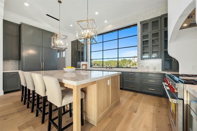 kitchen featuring light stone counters, stainless steel range, decorative light fixtures, a center island, and gray cabinets