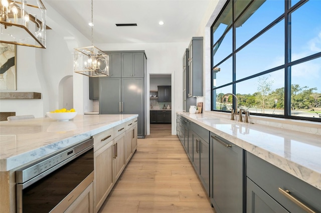 kitchen with light wood-type flooring, light stone counters, sink, pendant lighting, and gray cabinets