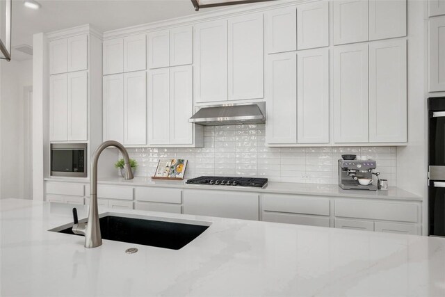 7501 Becasseau Dr, Austin, TX 78738 - kitchen featuring gas stovetop, ventilation hood, stainless steel microwave, tasteful backsplash, and white cabinetry