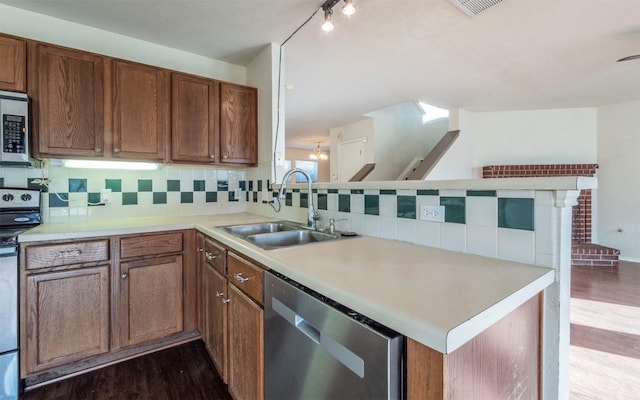 kitchen with kitchen peninsula, appliances with stainless steel finishes, decorative backsplash, dark wood-type flooring, and sink