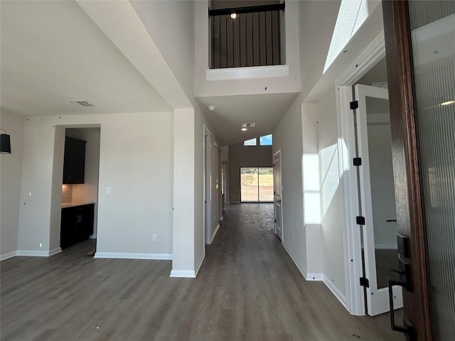 hall featuring a towering ceiling, baseboards, visible vents, and wood finished floors