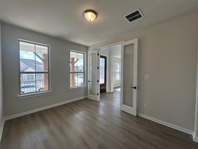 unfurnished room featuring baseboards, visible vents, and dark wood finished floors