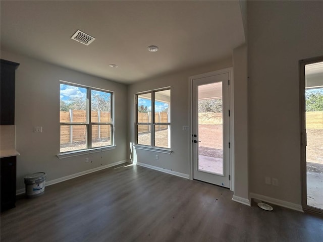 interior space with dark wood-type flooring, a healthy amount of sunlight, visible vents, and baseboards