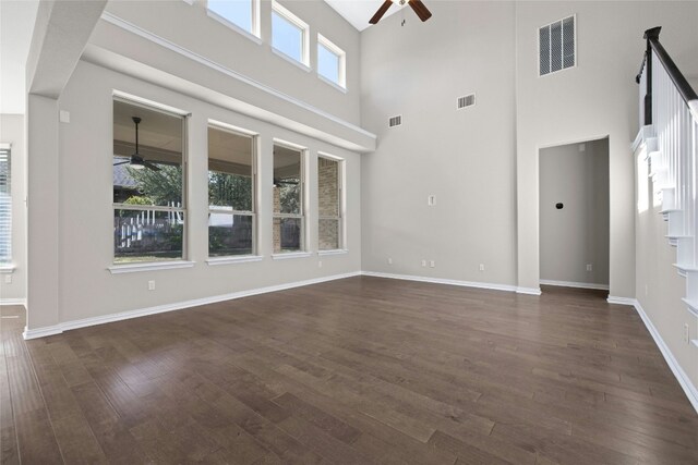 unfurnished living room with a high ceiling, dark wood-type flooring, and a healthy amount of sunlight