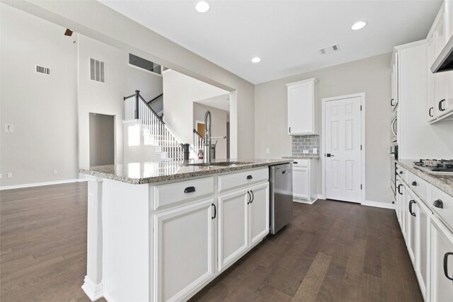 kitchen featuring dark wood-type flooring, a center island with sink, light stone counters, white cabinetry, and stainless steel appliances