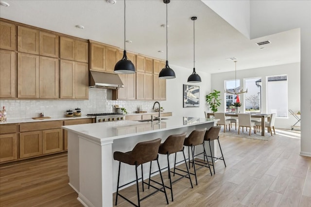 kitchen with sink, an island with sink, pendant lighting, extractor fan, and light wood-type flooring