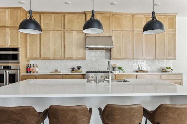 kitchen featuring decorative backsplash, light brown cabinetry, an island with sink, and decorative light fixtures