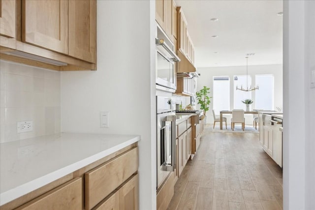 kitchen with stainless steel oven, light brown cabinets, an inviting chandelier, light hardwood / wood-style floors, and hanging light fixtures