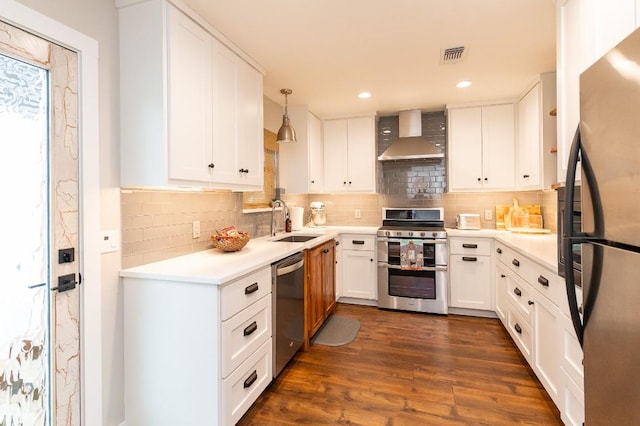 kitchen with white cabinetry, sink, wall chimney range hood, decorative light fixtures, and appliances with stainless steel finishes