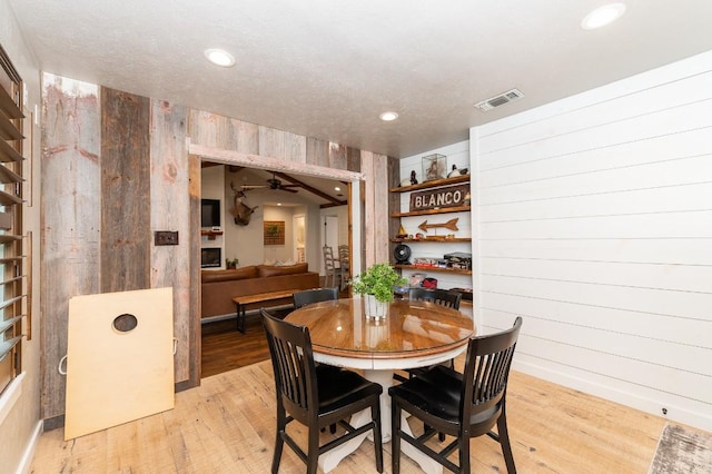 dining area with light wood-type flooring, ceiling fan, and wooden walls