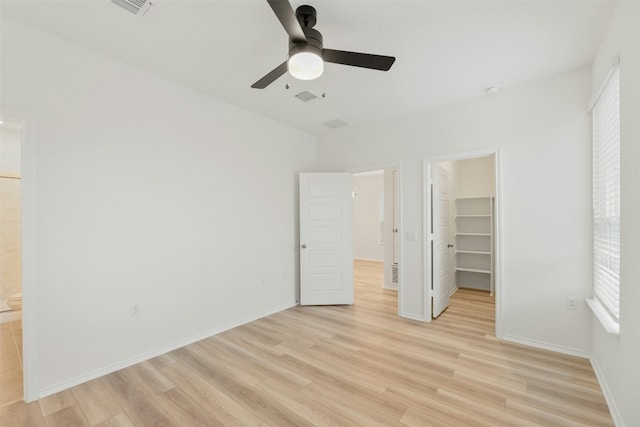 unfurnished bedroom with a walk in closet, ensuite bathroom, ceiling fan, light hardwood / wood-style floors, and a closet