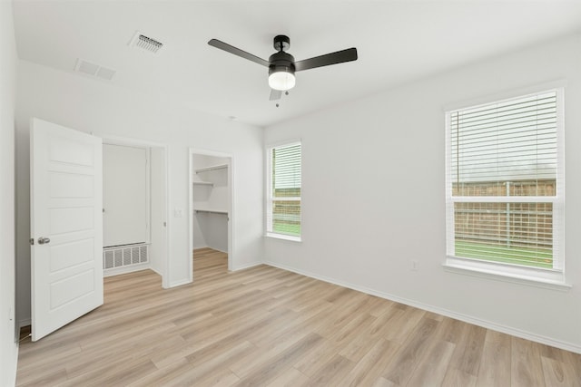 unfurnished bedroom with ceiling fan, a walk in closet, and light hardwood / wood-style flooring