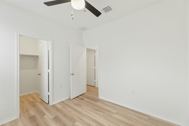 unfurnished bedroom with ceiling fan, a closet, a spacious closet, and light wood-type flooring