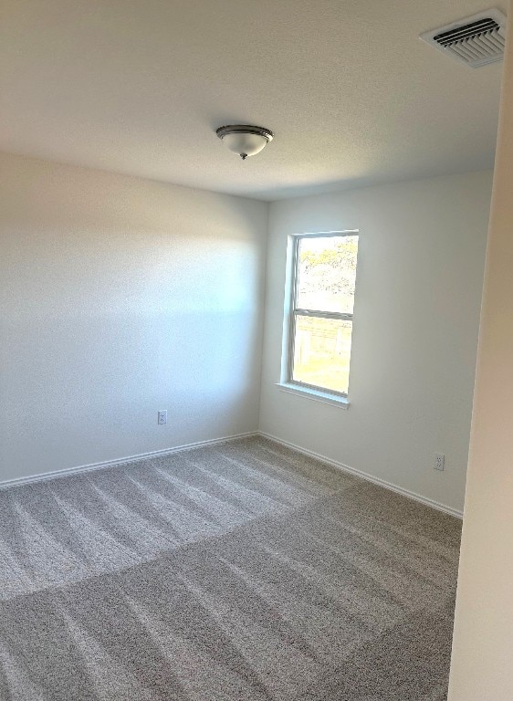 carpeted spare room with baseboards, visible vents, and a textured ceiling