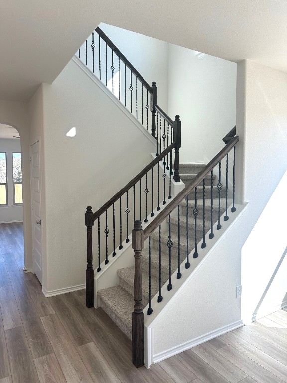 staircase with baseboards, arched walkways, and wood finished floors