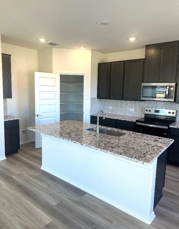 kitchen with a sink, visible vents, appliances with stainless steel finishes, light stone countertops, and tasteful backsplash