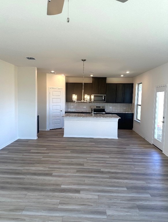 kitchen featuring light wood-type flooring, stainless steel appliances, decorative backsplash, and an island with sink