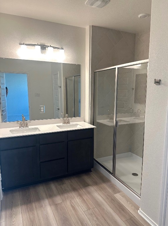 bathroom featuring a textured wall, a shower stall, a sink, and wood finished floors