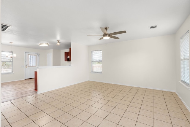 unfurnished room featuring light tile patterned floors and ceiling fan with notable chandelier