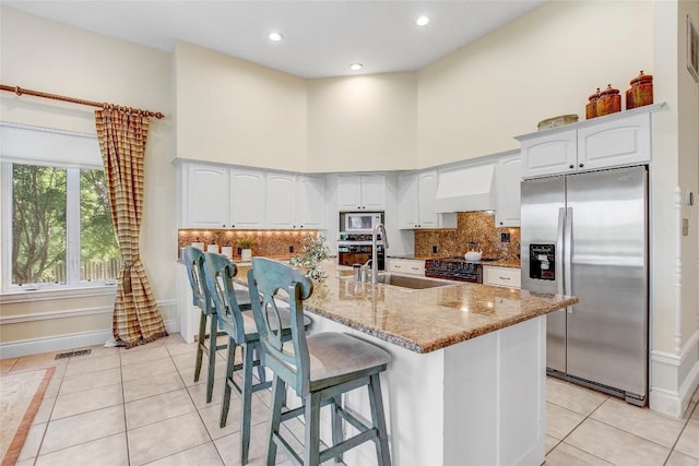 13628 Gregg Manor Rd, Manor, TX 78653 - kitchen featuring appliances with stainless steel finishes, custom exhaust hood, a sink, light tile patterned flooring, and light stone counters