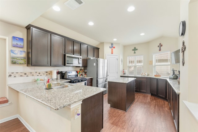 kitchen with kitchen peninsula, light stone countertops, stainless steel appliances, and a kitchen island