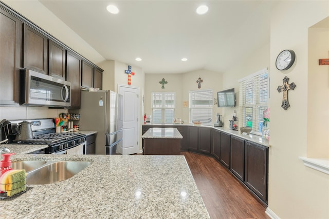 kitchen with light stone countertops, a wealth of natural light, stainless steel appliances, and dark brown cabinets