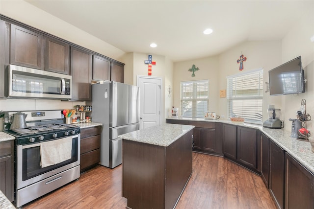 kitchen featuring light stone countertops, appliances with stainless steel finishes, a kitchen island, dark hardwood / wood-style floors, and dark brown cabinets