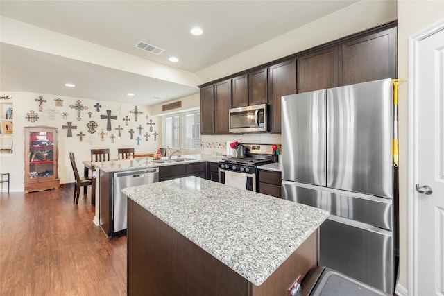 kitchen with kitchen peninsula, appliances with stainless steel finishes, dark brown cabinets, light stone countertops, and a kitchen island