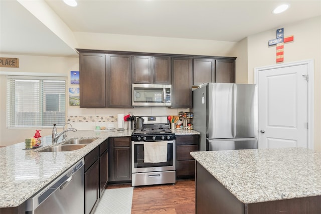 kitchen with dark brown cabinetry, appliances with stainless steel finishes, a center island, sink, and light stone counters