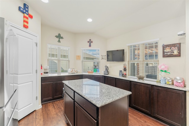 kitchen with light stone countertops, dark hardwood / wood-style flooring, dark brown cabinets, and a center island