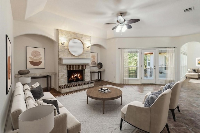 living room featuring ceiling fan, a stone fireplace, french doors, and a tray ceiling