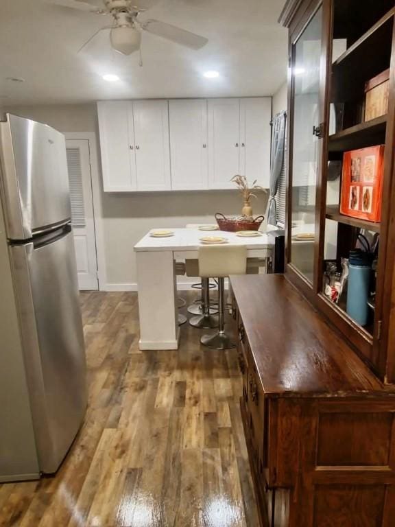 kitchen with stainless steel fridge, ceiling fan, dark wood-type flooring, white cabinets, and a kitchen island