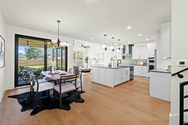 dining area featuring sink, ceiling fan with notable chandelier, and light hardwood / wood-style floors