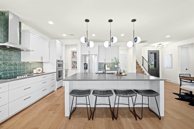 kitchen with wall chimney exhaust hood, sink, a center island with sink, appliances with stainless steel finishes, and white cabinets