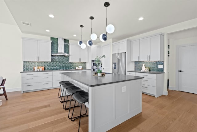 kitchen featuring white cabinets, hanging light fixtures, a center island, high end fridge, and wall chimney exhaust hood