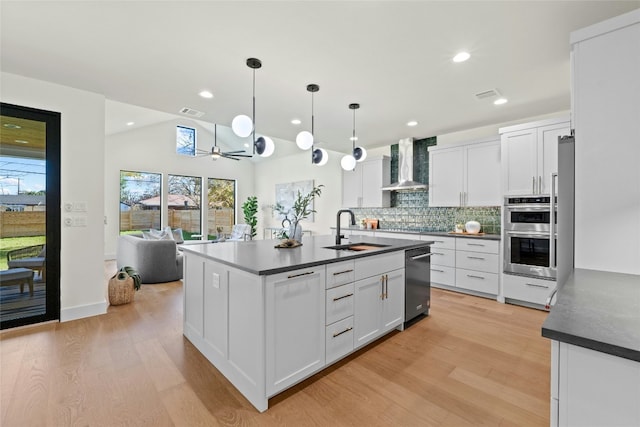 kitchen featuring white cabinetry, sink, decorative light fixtures, and wall chimney range hood