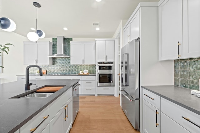 kitchen featuring wall chimney exhaust hood, sink, decorative light fixtures, stainless steel appliances, and white cabinets