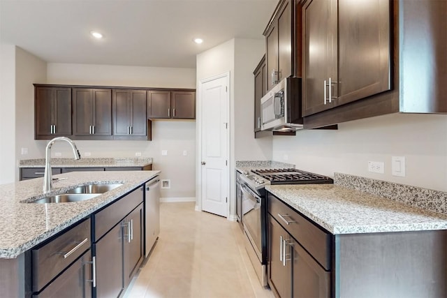 kitchen with light stone countertops, appliances with stainless steel finishes, dark brown cabinetry, sink, and light tile patterned floors