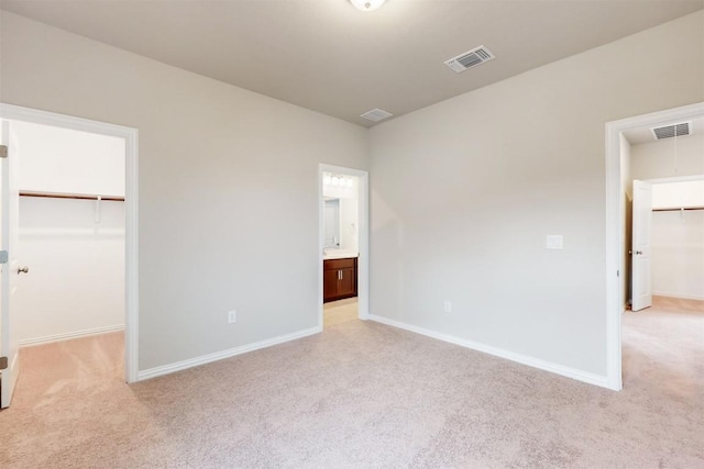 unfurnished bedroom featuring light carpet, a walk in closet, ensuite bathroom, and a closet