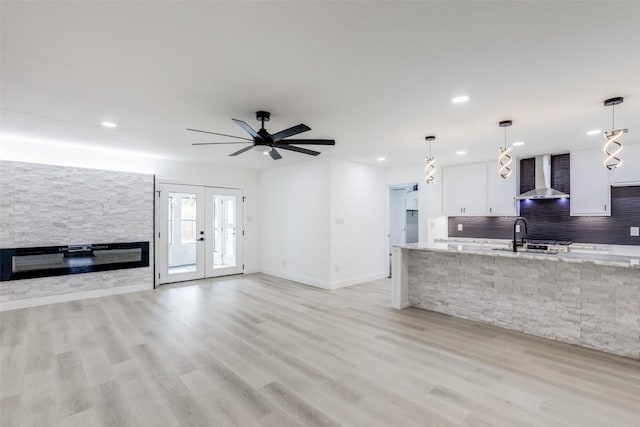 kitchen with ceiling fan, sink, wall chimney range hood, white cabinets, and hanging light fixtures