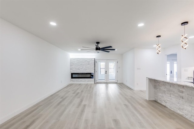 unfurnished living room with ceiling fan, a stone fireplace, light wood-type flooring, and french doors