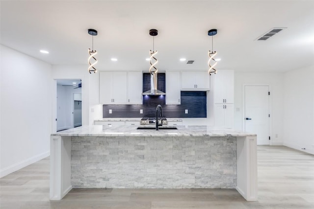 kitchen with pendant lighting, a large island, light stone countertops, and wall chimney range hood