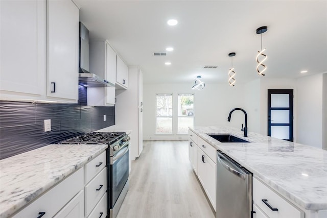 kitchen with stainless steel appliances, sink, wall chimney range hood, pendant lighting, and white cabinets