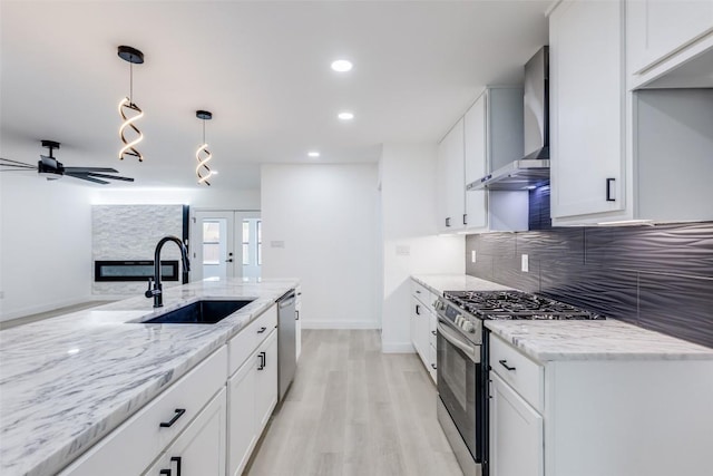 kitchen with white cabinets, wall chimney range hood, sink, hanging light fixtures, and appliances with stainless steel finishes