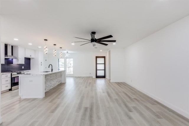 kitchen with a kitchen island with sink, white cabinets, wall chimney range hood, decorative light fixtures, and gas stove