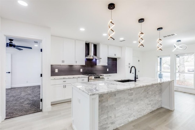 kitchen with a kitchen island with sink, white cabinets, sink, wall chimney exhaust hood, and stainless steel range oven